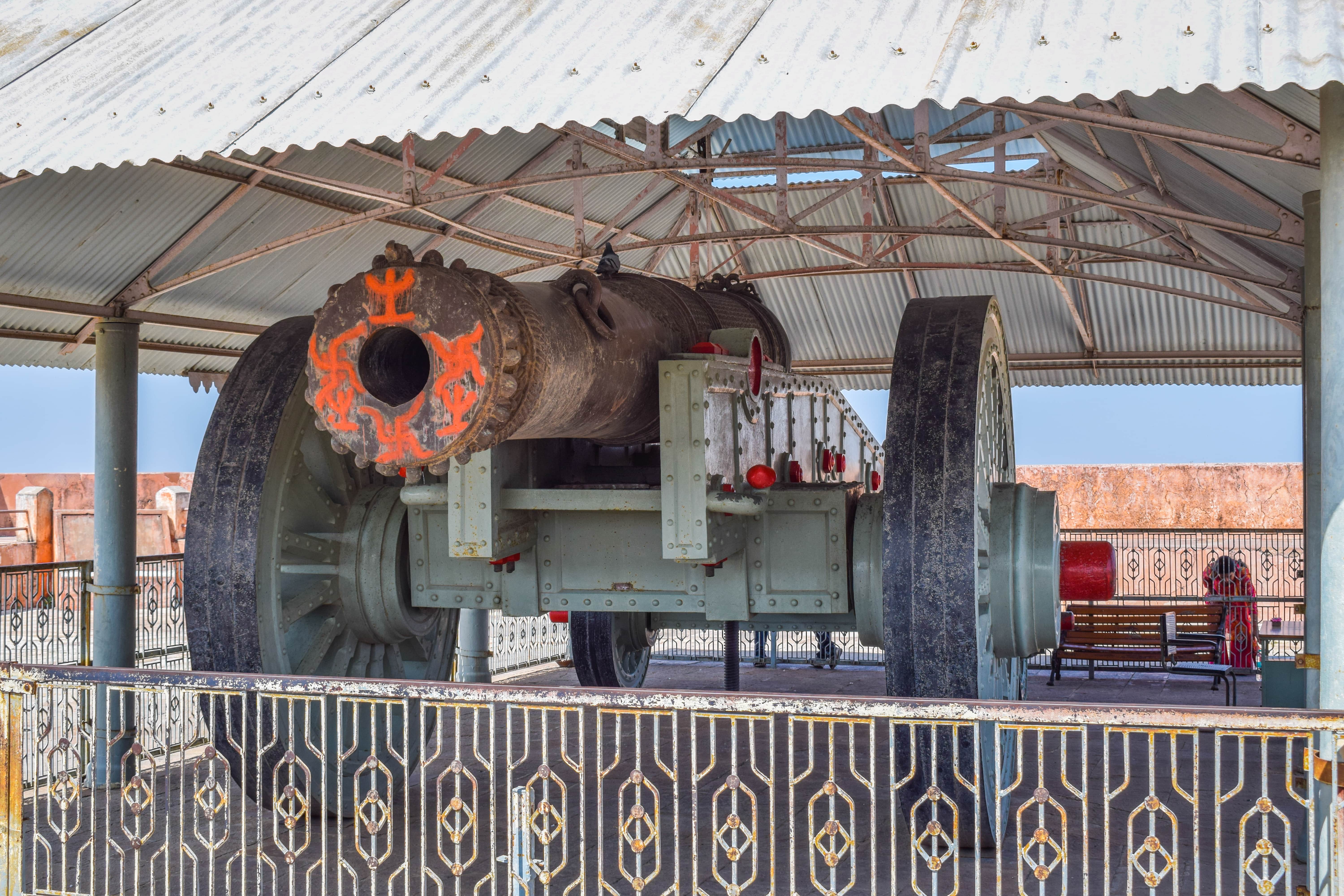 The massive Jaivana Cannon, once the world's largest cannon on wheels, displayed under a shed at Jaigarh Fort, Jaipur, Rajasthan, with orange ceremonial markings on its muzzle.